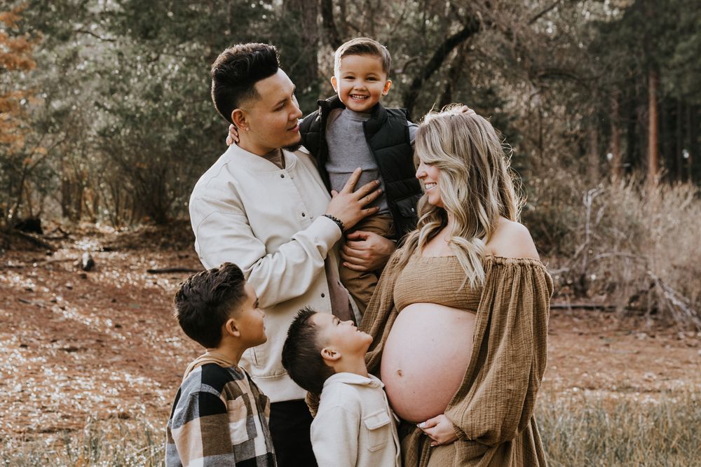 A dad launches his boy into the air as his wife and kids look on in the sunlit forest outside of Sacramento during a family photo shoot.