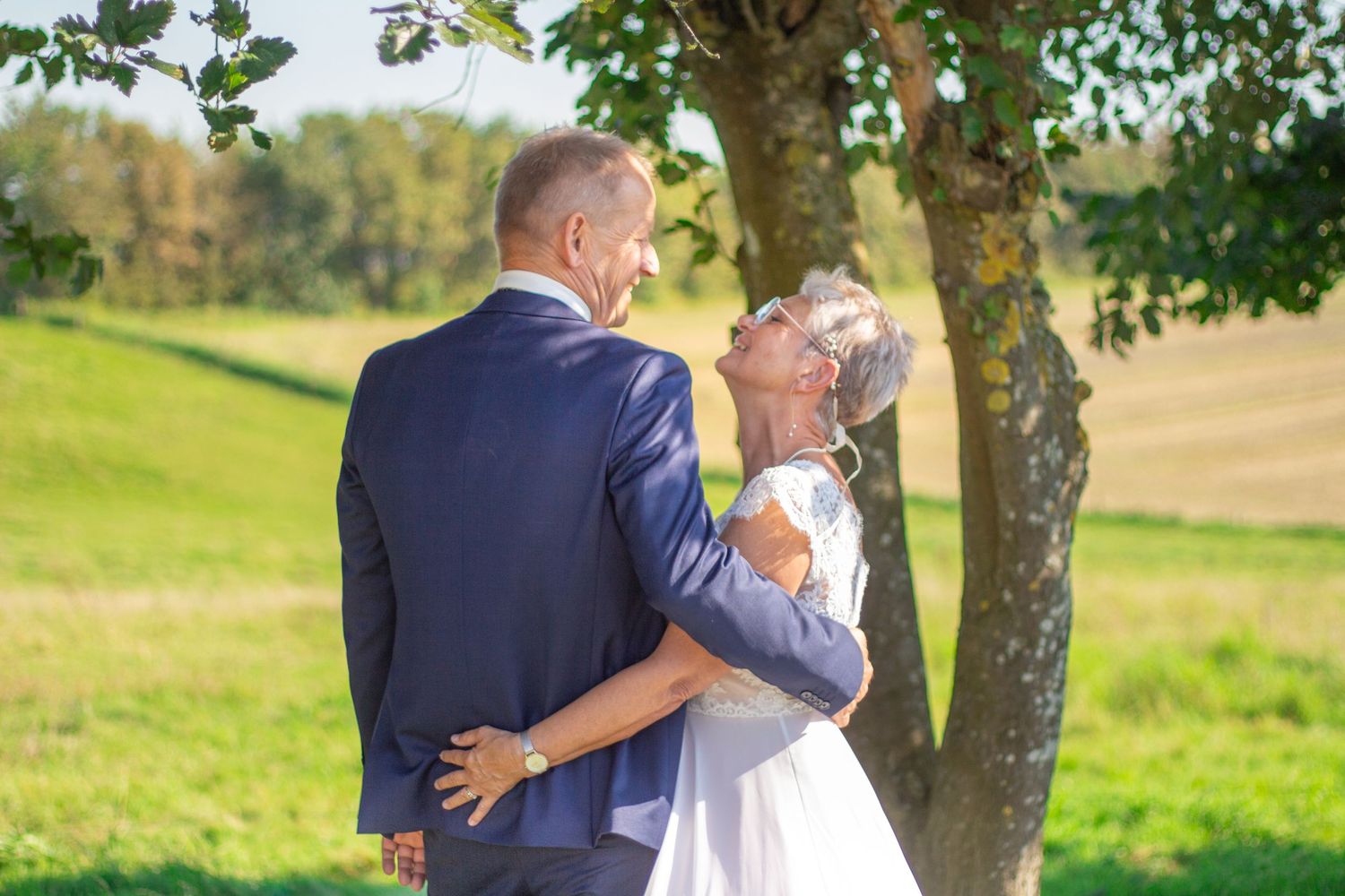 Wedding couple embracing under tree with golden sunlight streaming through branches.
