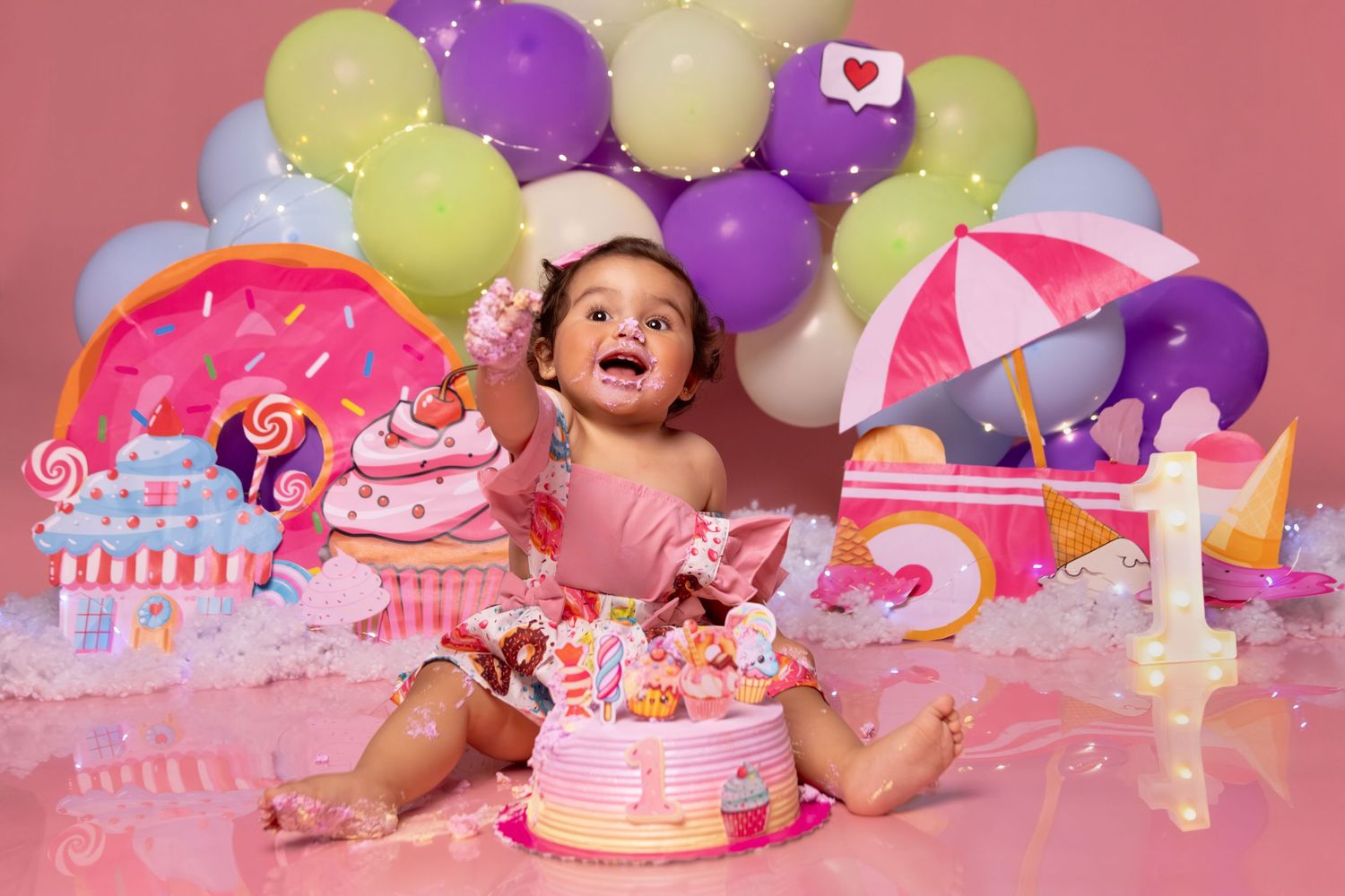 Colorful cake smash setup with pink and purple balloons and birthday cake decorations.