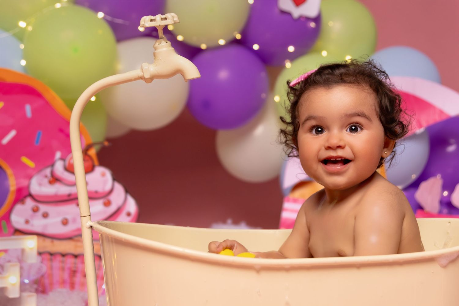 Festive birthday setup with purple and yellow balloons against a pink backdrop for a cake smash photoshoot.