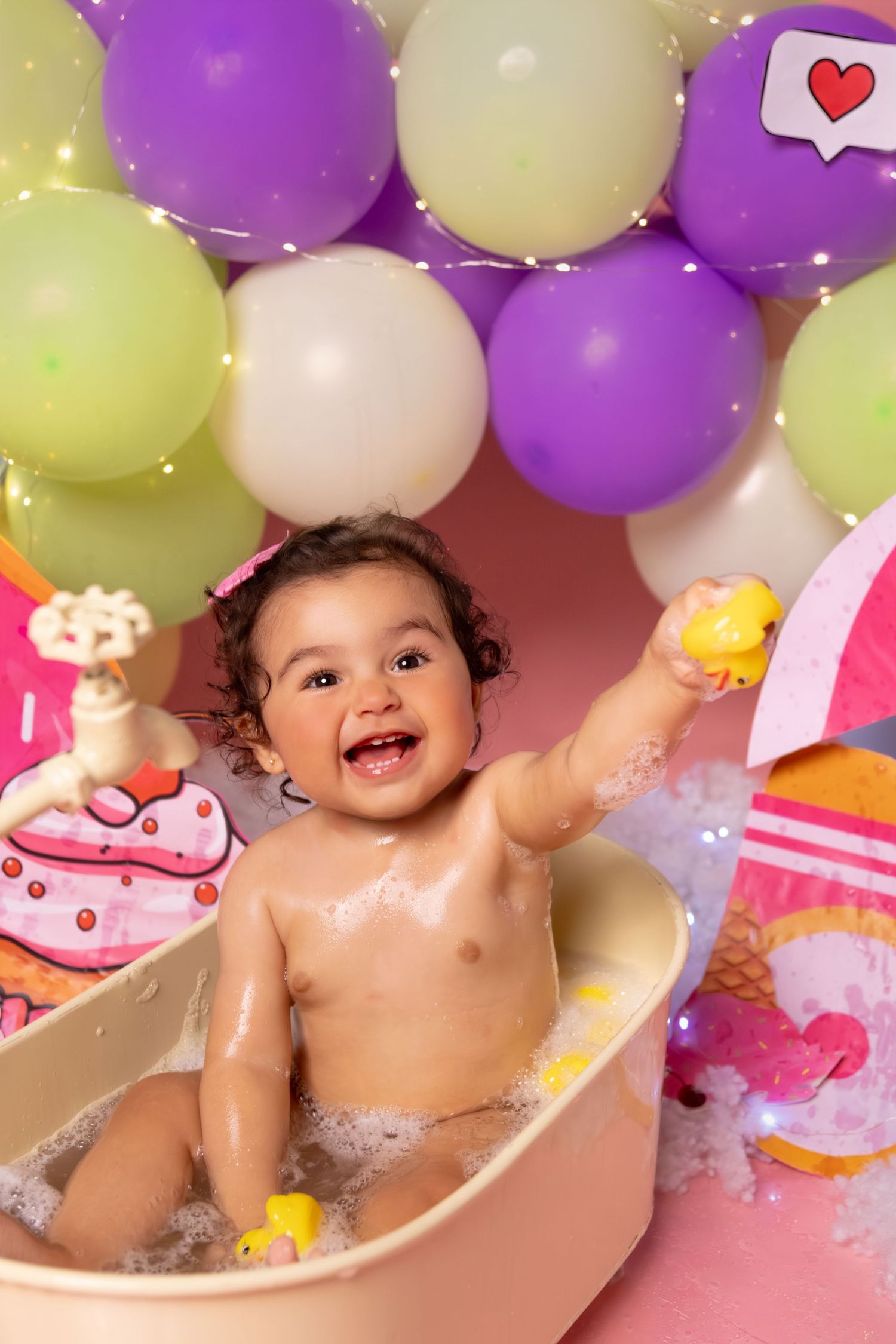 Baby enjoying a cake smash photoshoot surrounded by colorful balloons and decorative elements.