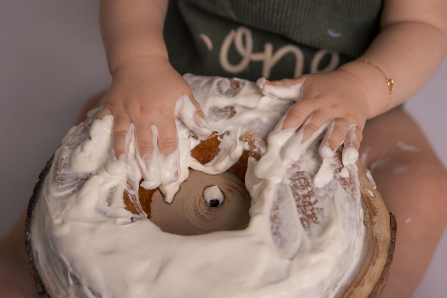 Small hands playing with white frosting on chocolate cake during cake smash session.