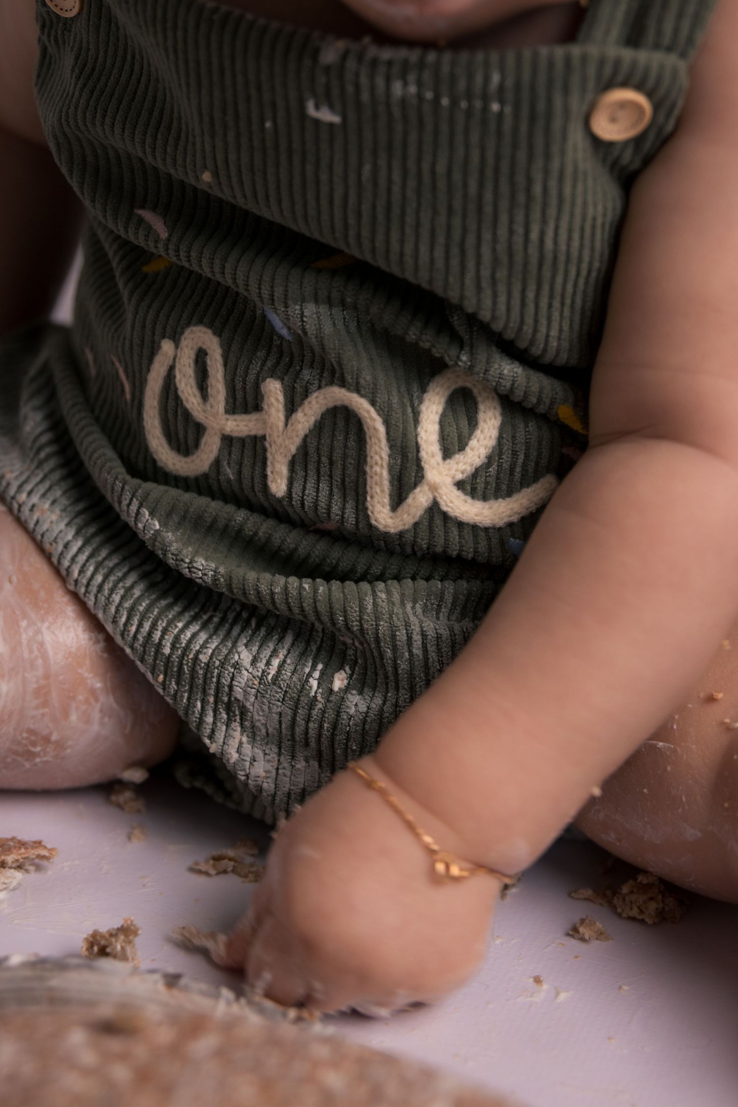 Detail shot of corduroy overalls with 'one' text and gold glitter on floor.