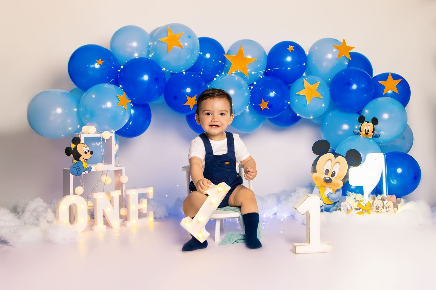 Mickey Mouse themed first birthday setup with blue balloon arch and decorative props.