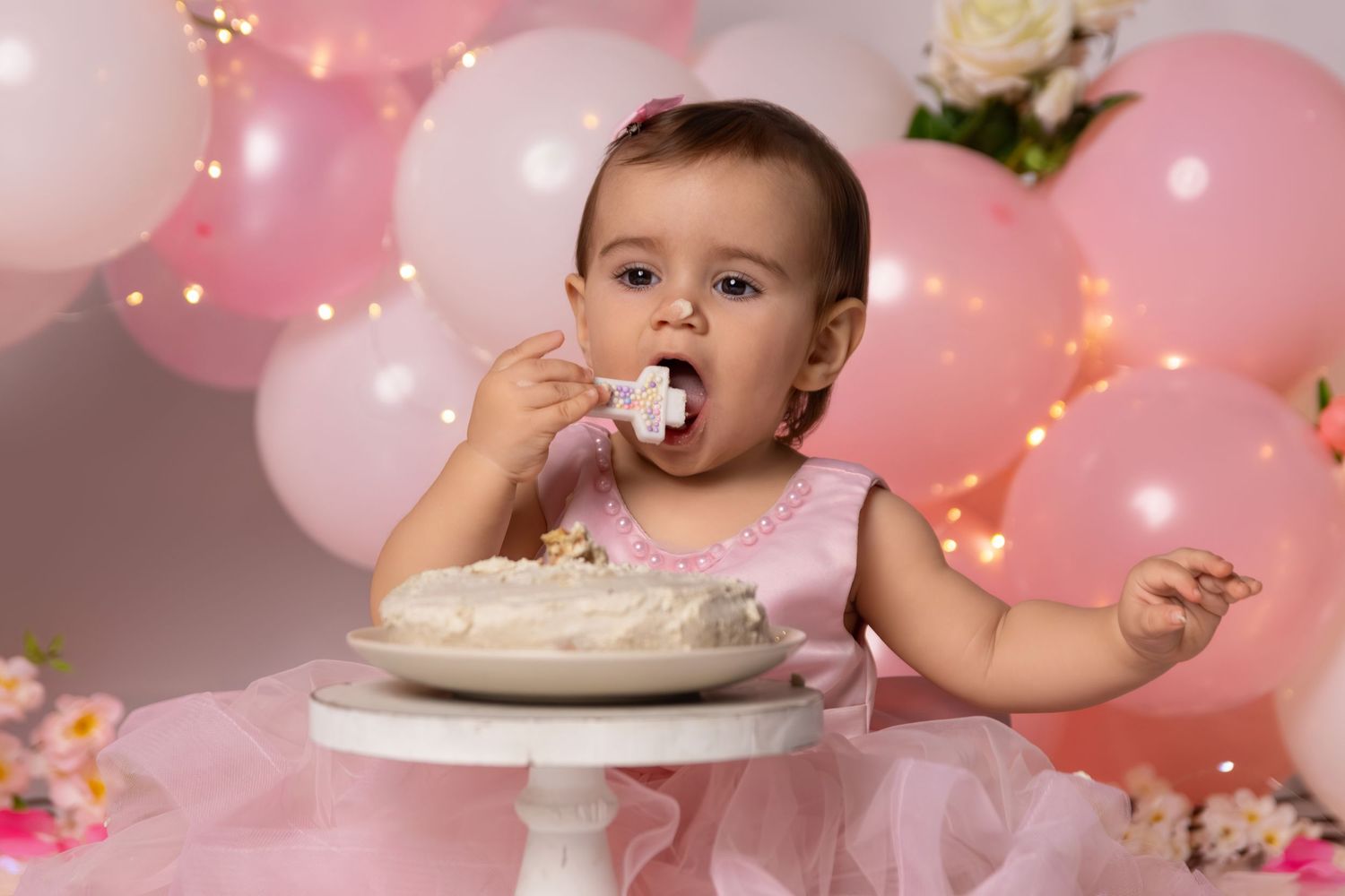 Cake smash photography session with pink balloons and string lights for first birthday celebration.