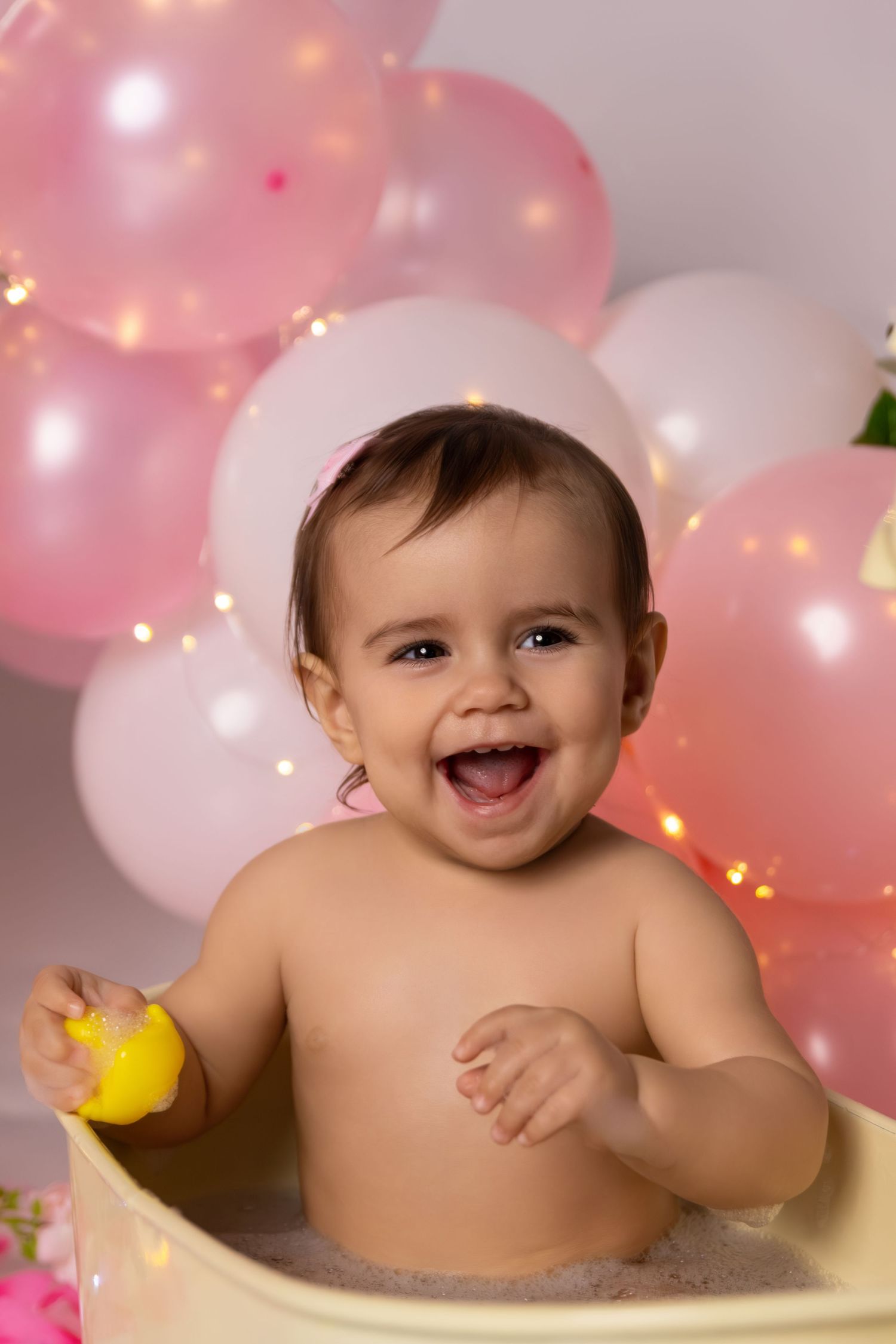 Baby bath photography with yellow duck toy against pink balloon background.