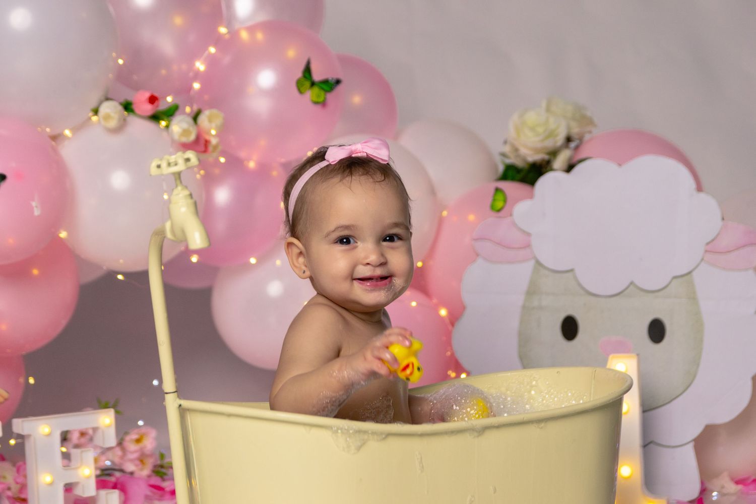Pink balloon arch and decorative setup for a cake smash photo session with white clouds and gold accents.