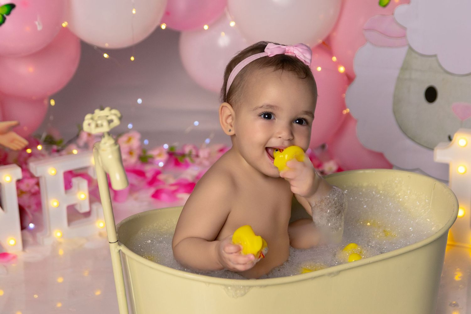 Bath time photography setup with cream-colored tub and pink balloon background.