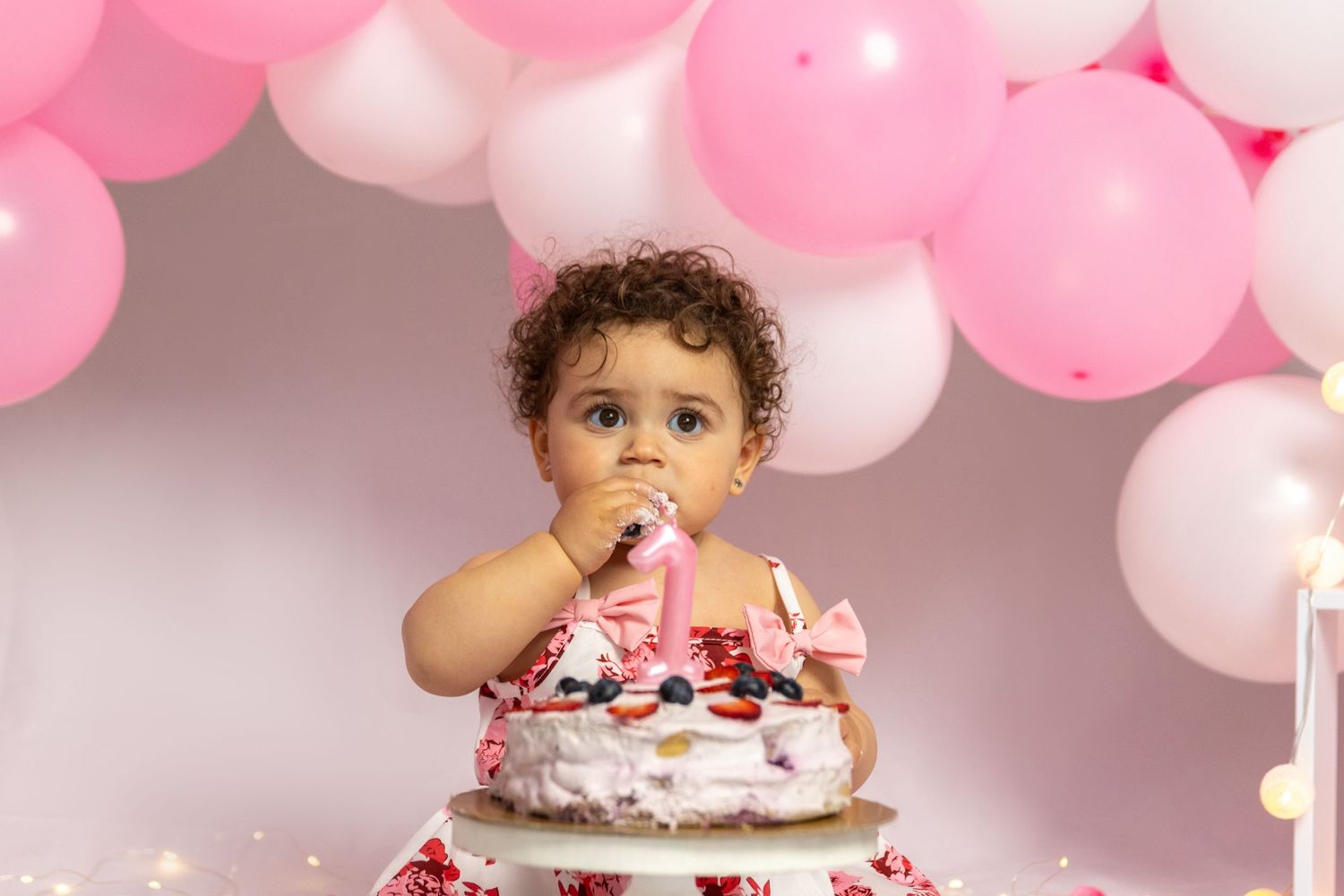 A cake smash photo session with pink and white balloons in the background.