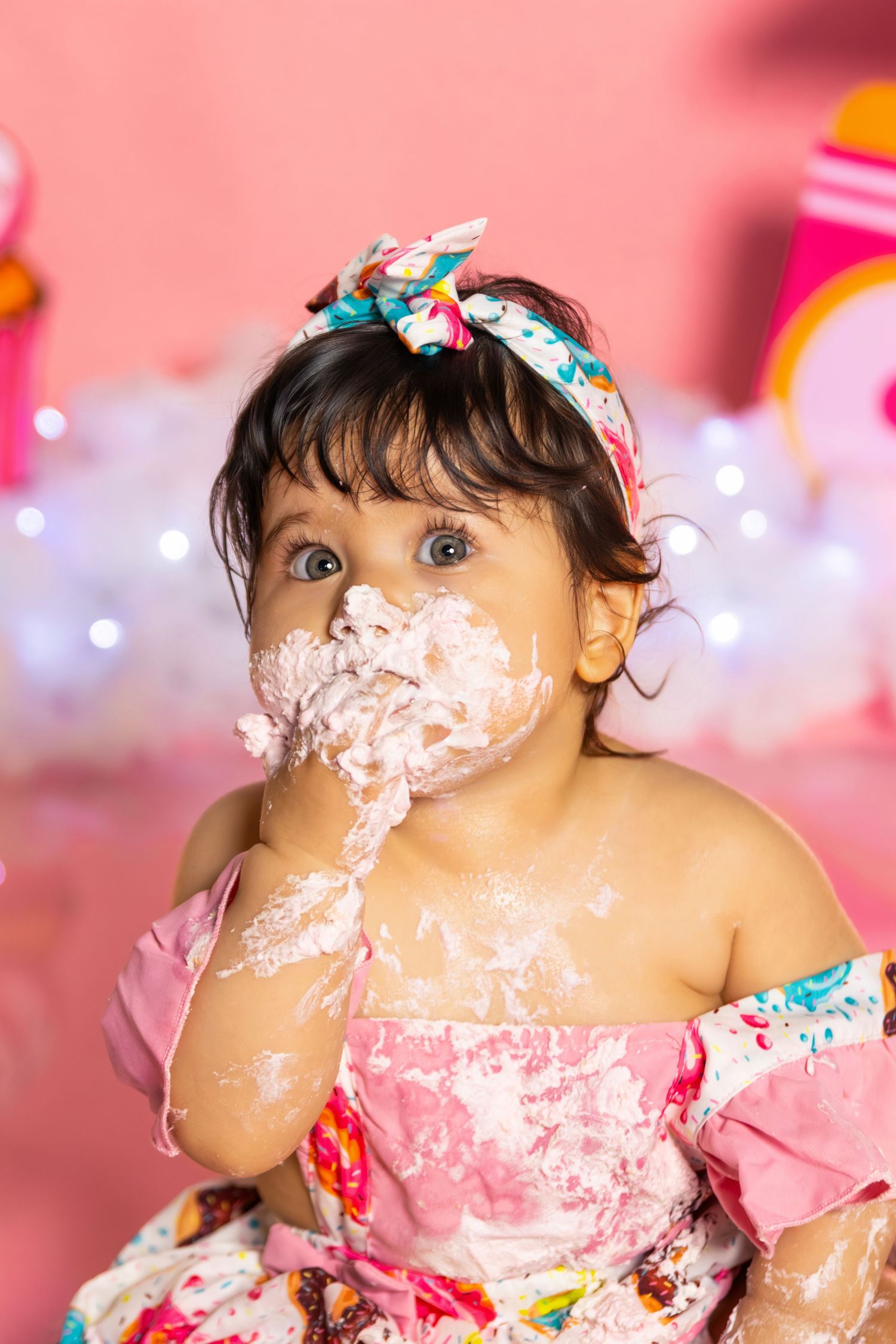 Cake smash photo session with pink backdrop and twinkling lights.