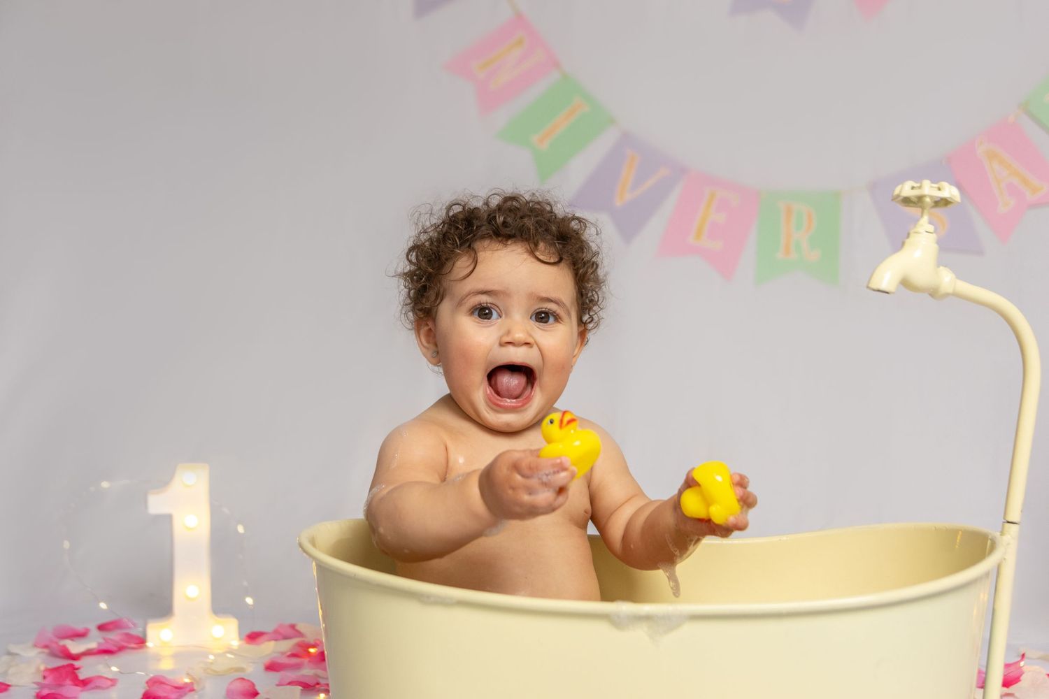 A festive first birthday setup with a yellow bathtub and colorful bunting decorations.