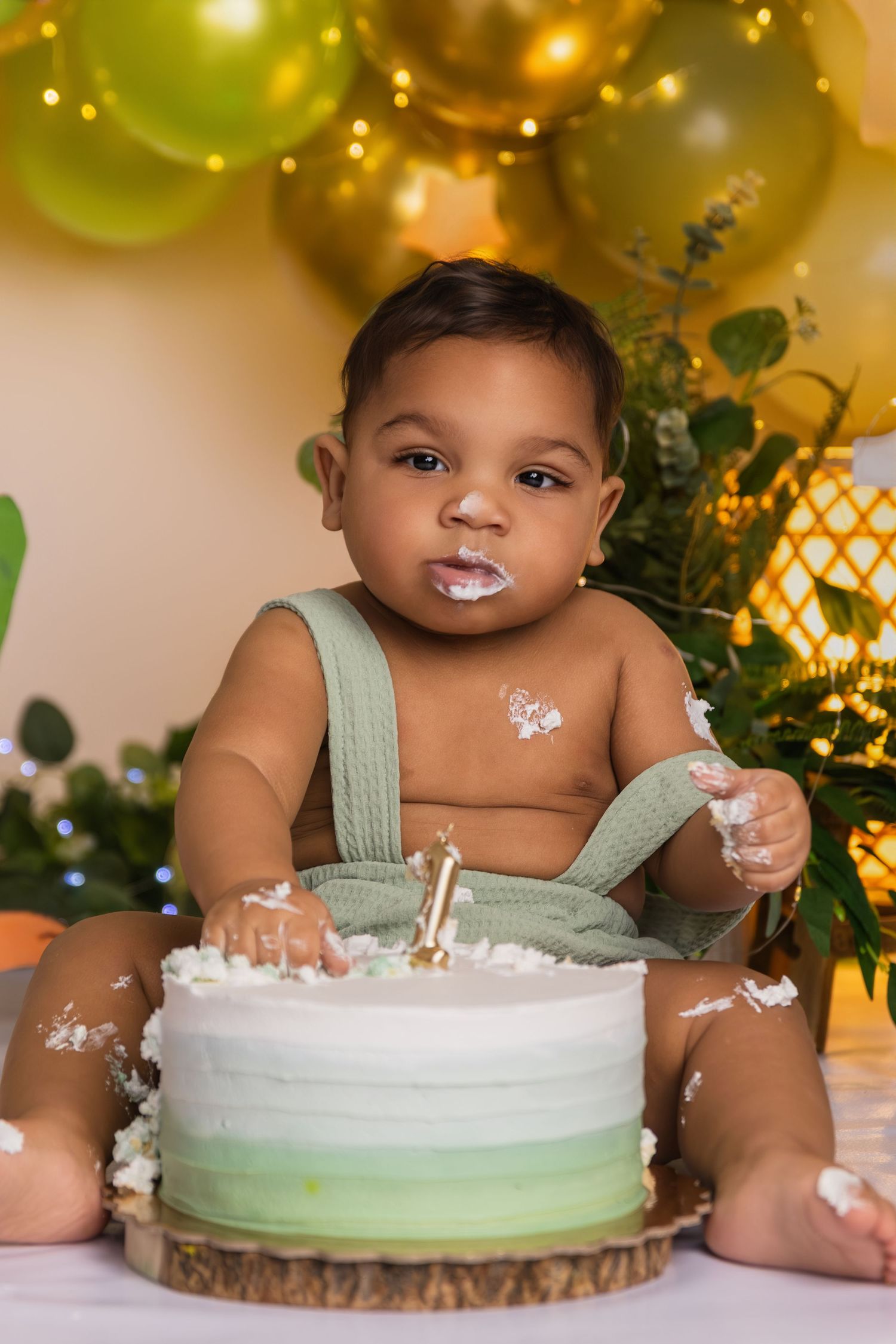 Cake smash photo session with mint green and white cake on wooden slice with balloon decor.