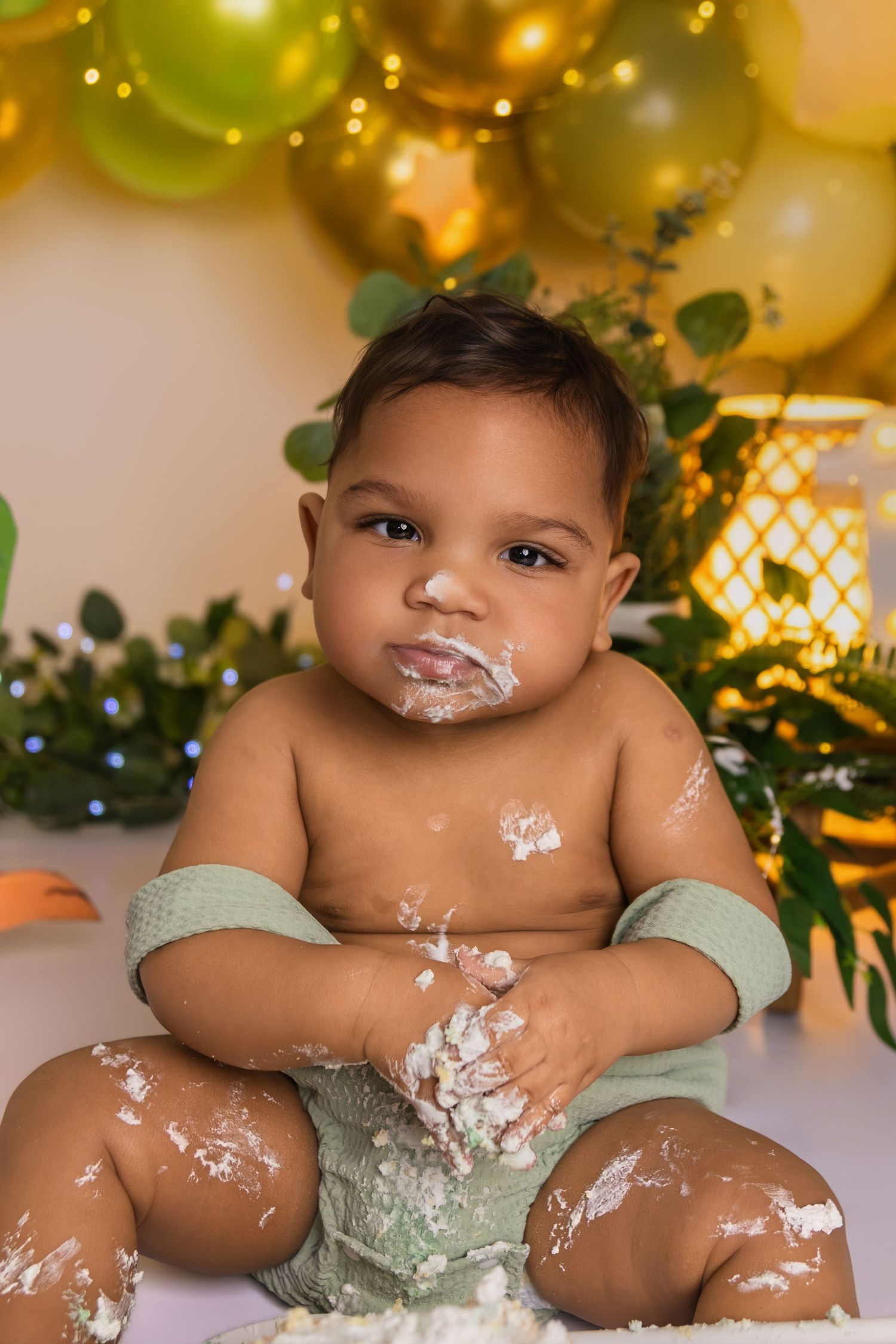 Messy cake smash photography session with frosting covered baby and festive backdrop.