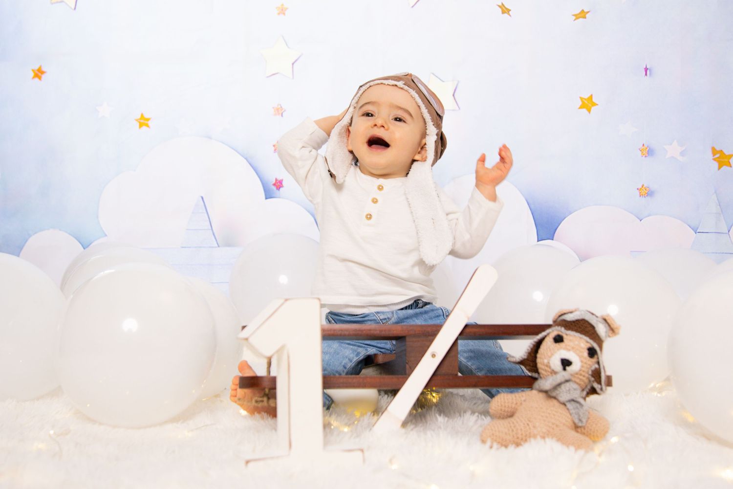 First birthday photo setup with white clouds, number one prop, and stuffed animal.