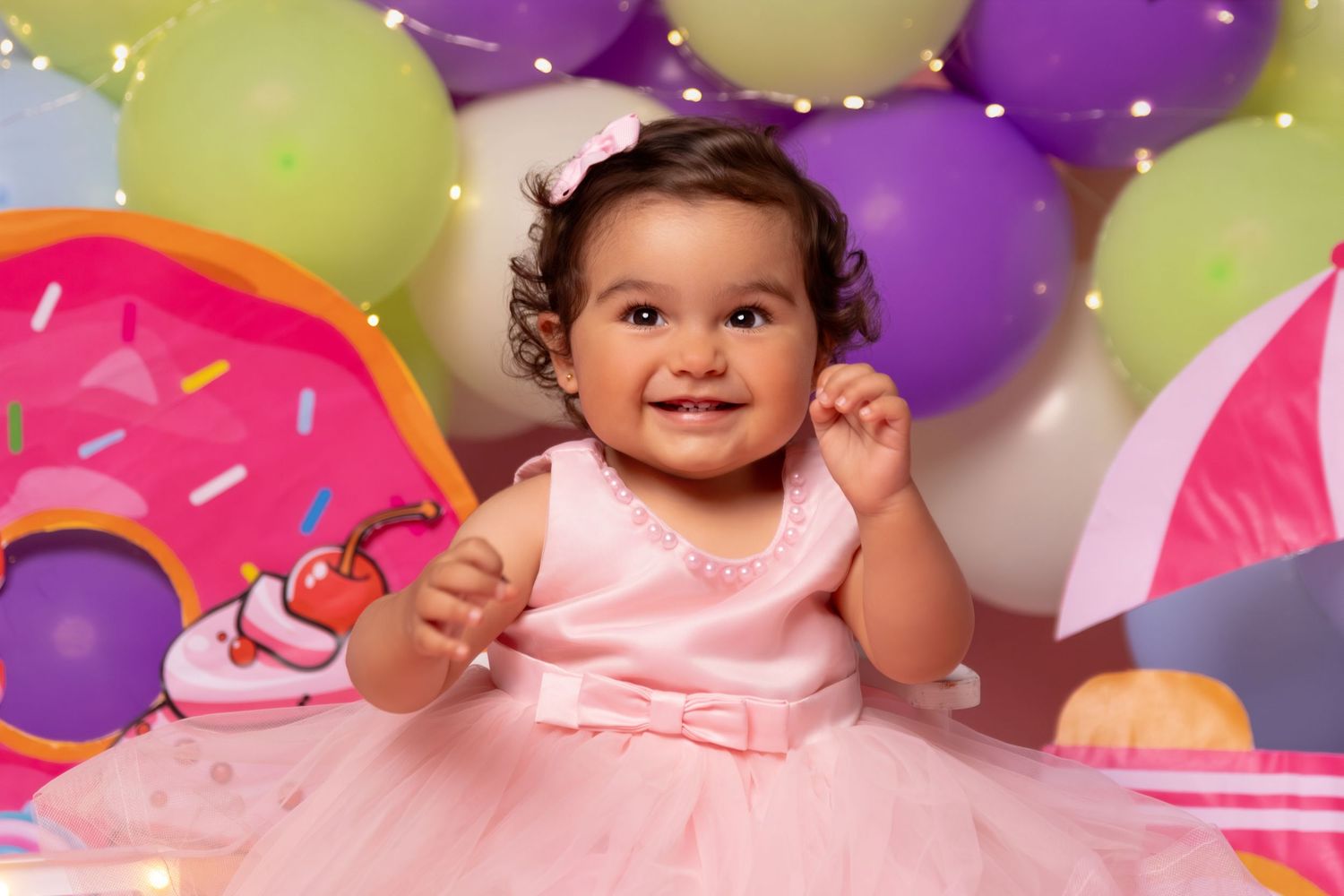 Colorful birthday photo setup with purple and yellow balloons against pink background.