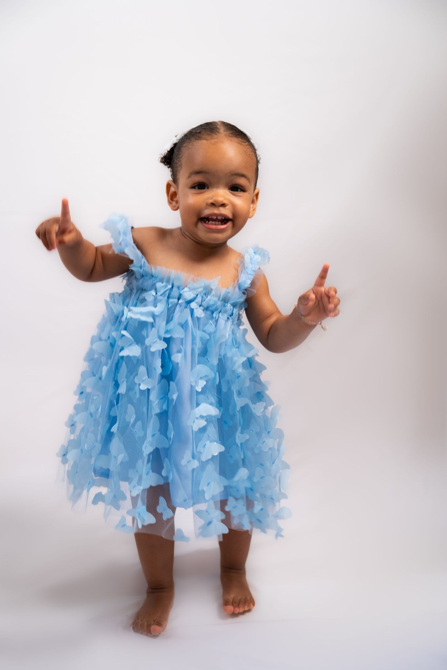 Toddler in light blue tulle dress dancing and posing against white background.