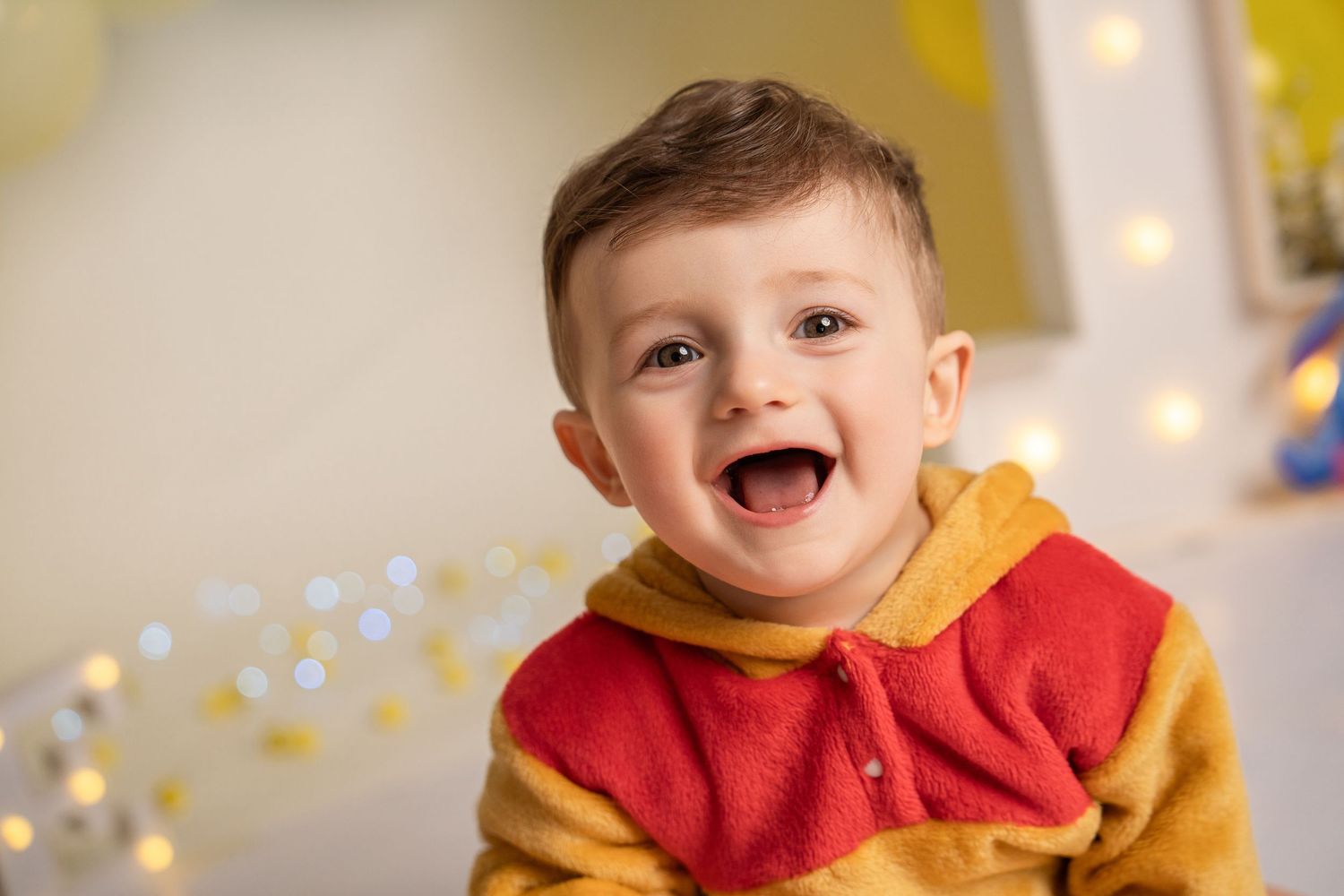 Happy toddler boy in Winnie the Pooh costume laughing joyfully with bokeh lights in background.