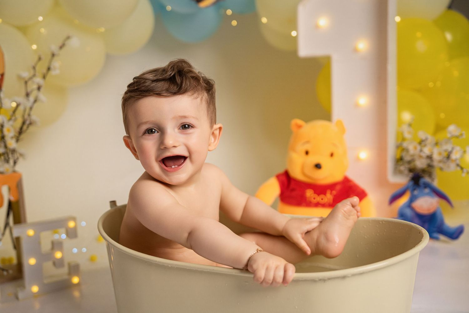 Happy baby boy laughing in cream tub at Winnie the Pooh themed first birthday cake smash session.