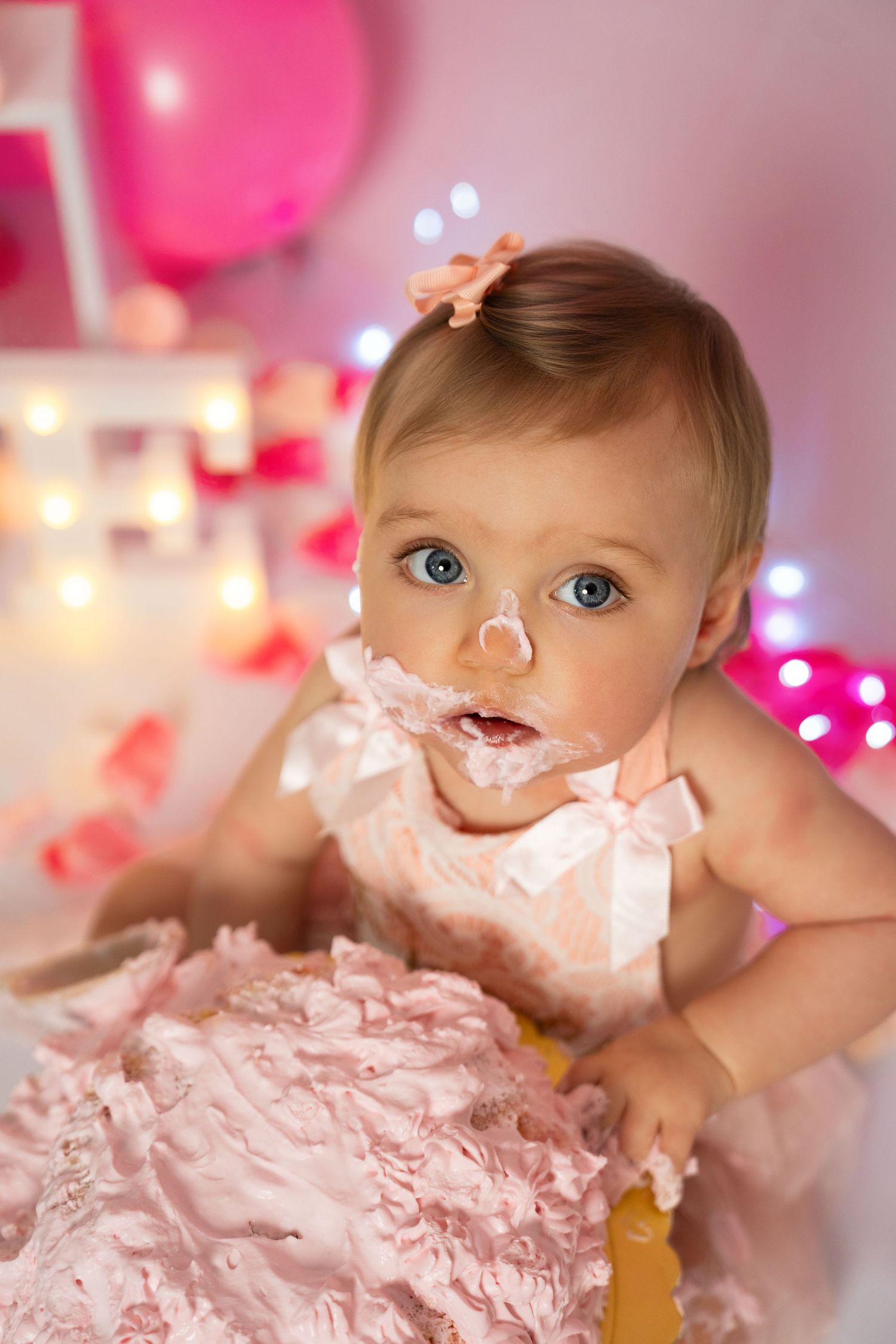 Baby with cake frosting on face during cake smash photo session with pink decorations.