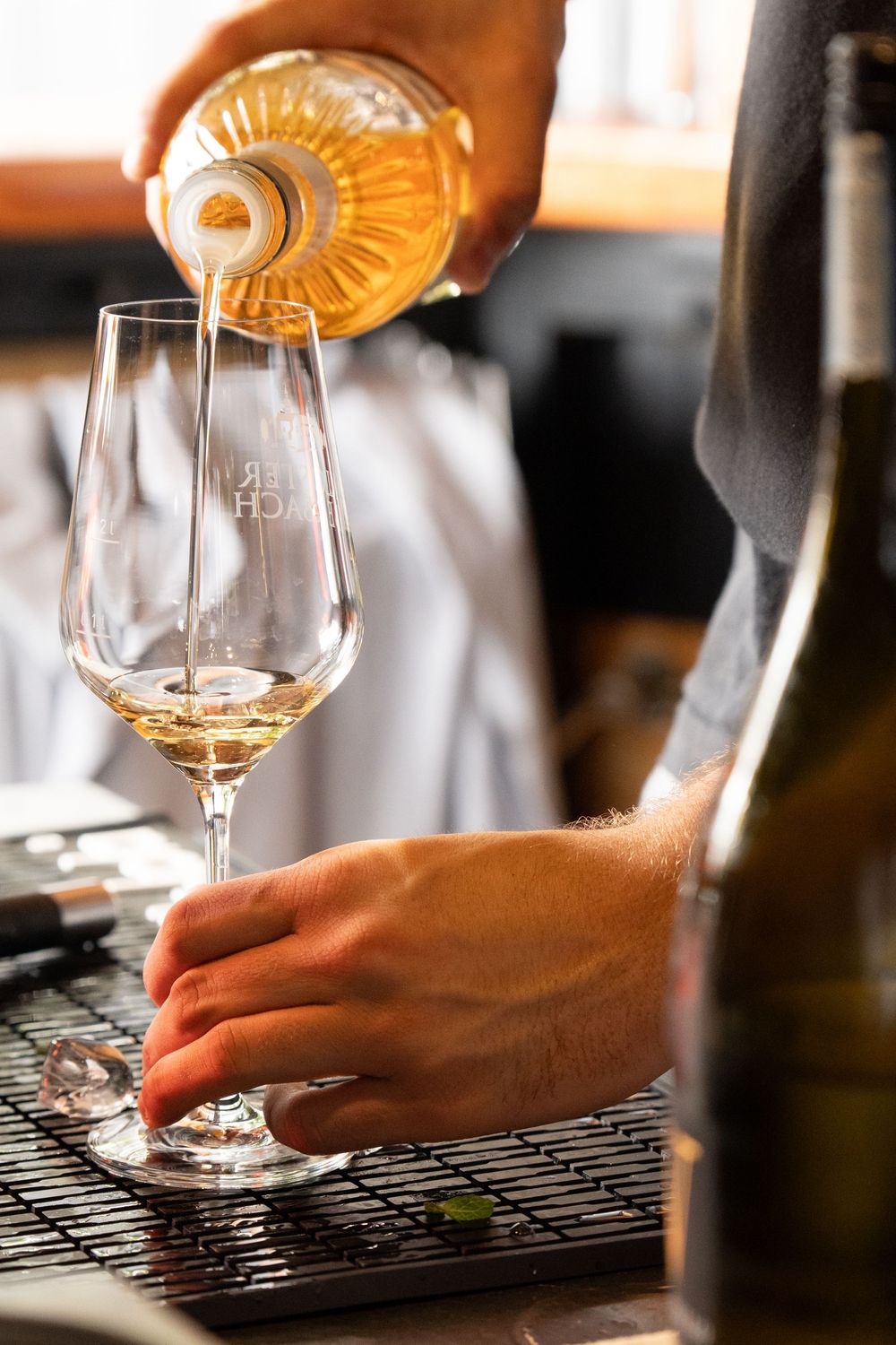 A series of wine tasting glasses being filled with golden liquid on a dark surface in a restaurant setting.