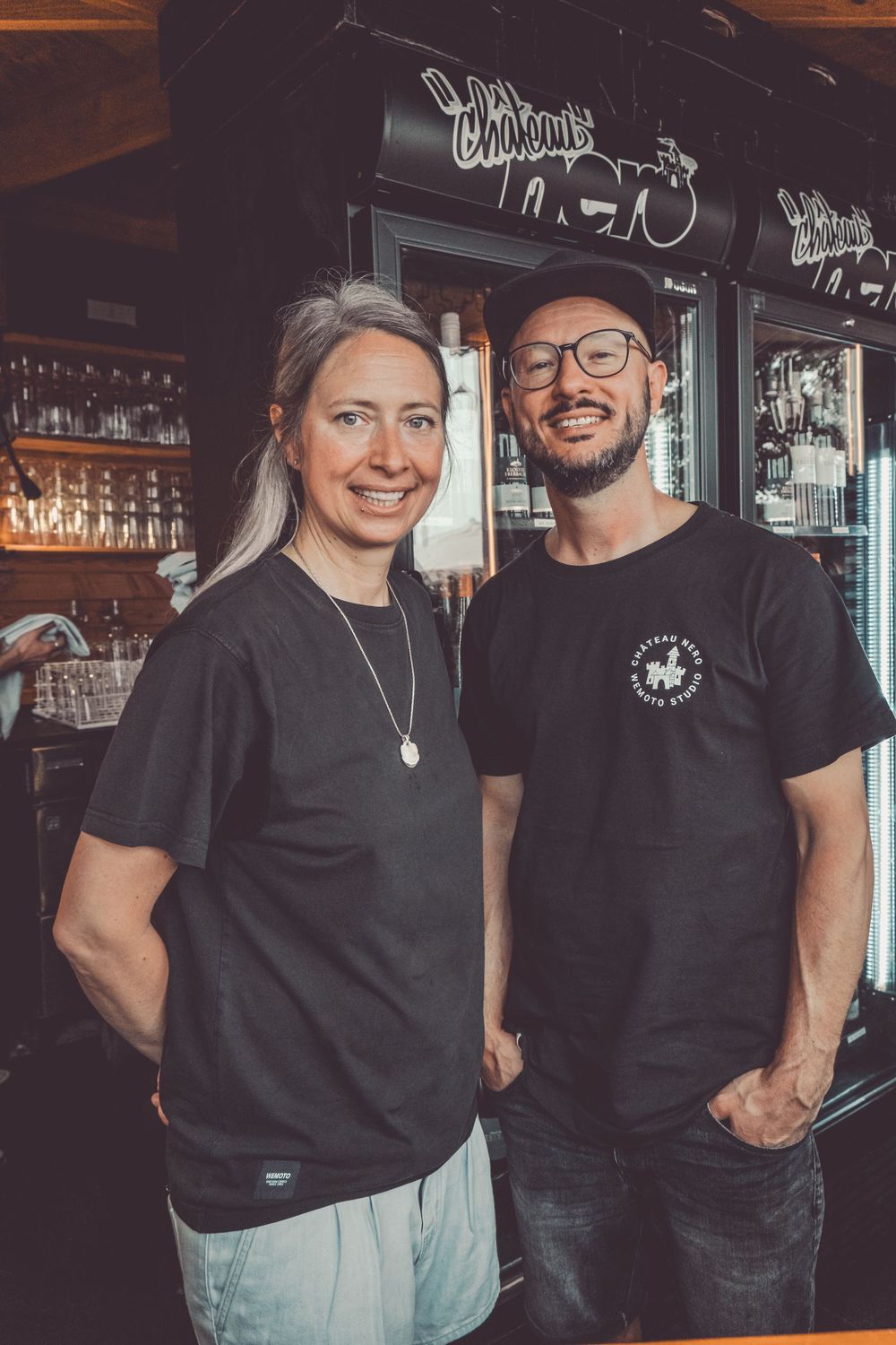 People in black t-shirts gathered at a bar counter in a casual restaurant setting.