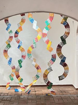 Curved installation of  woven plastic rainbow-colored hanging elements creating wave patterns through archway.