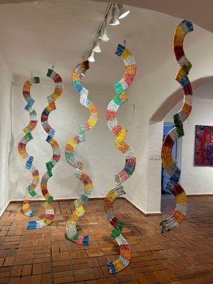 Hanging sculptural installation with colorful wavy woven plastic ribbons suspended from gallery ceiling.