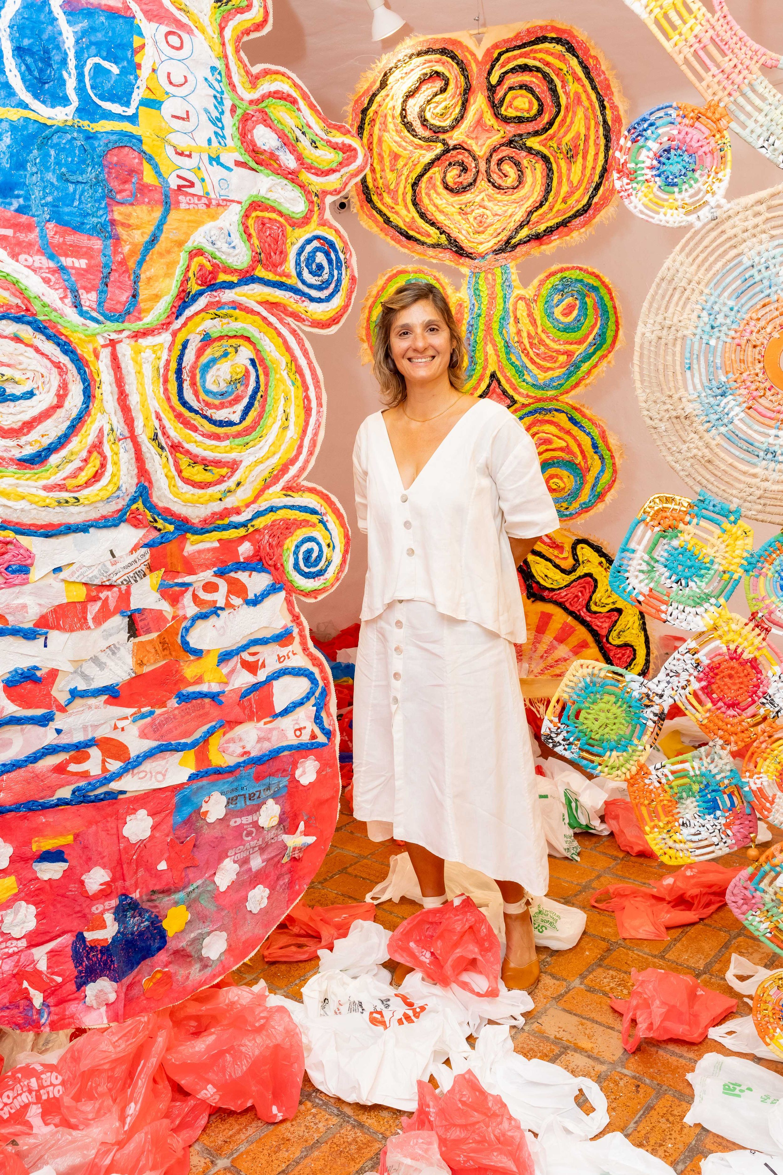 Woman in white dress stands among colorful swirling abstract art installations with plastic bag sculptures.