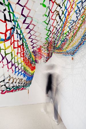 Colorful zigzag paper art installation creates dynamic patterns along corridor wall with blurred figure walking past.