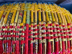 Colorful yellow and red rolled fabric scrolls with gold accents arranged in neat rows at a traditional market.