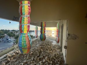 Colorful cylindrical art installations hanging in a damaged concrete space with city view.