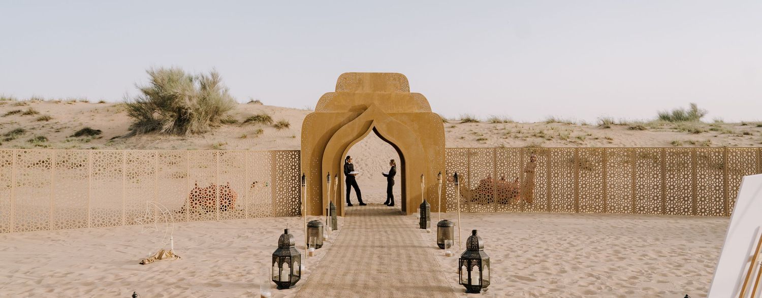 Desert archway entrance with sand dunes in background under bright sunlight.