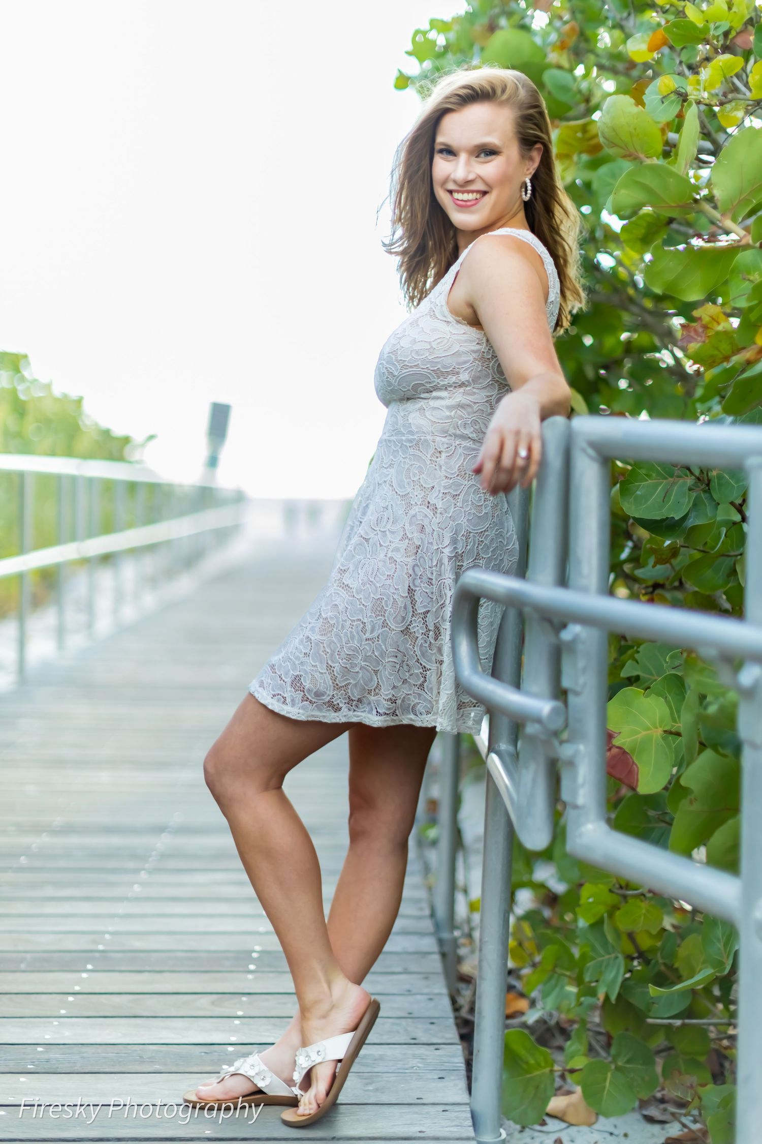 Figure in silver dress poses casually on wooden boardwalk near foliage.