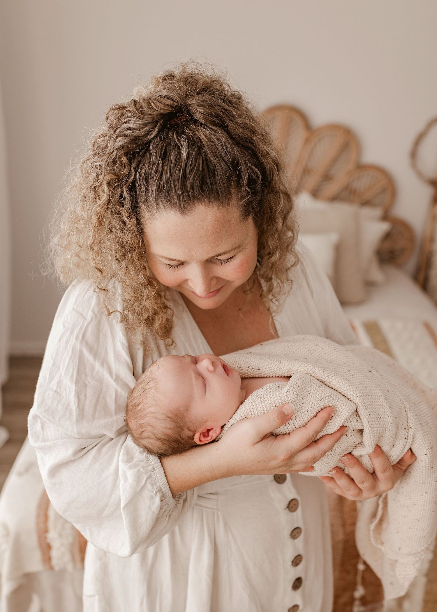 Mother in white dress tenderly holding newborn baby in intimate indoor portrait.