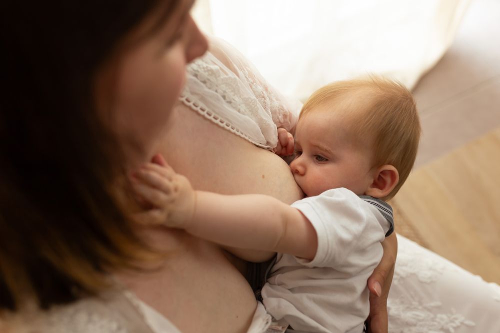 Détail d'un allaitement en studio avec la main de maman sur son bébé de 4 mois, portrait de maternité artistique et peau à peau à Niort.