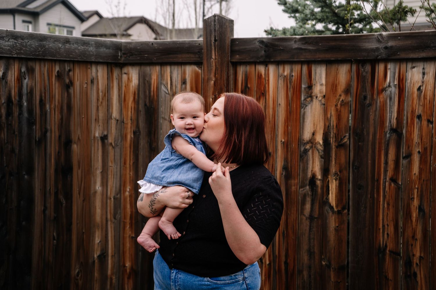 A tender moment shared between parent and baby against a wooden fence backdrop.