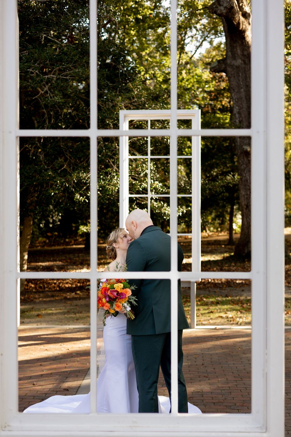 A romantic wedding scene with white columns and windows frames the couple during their special moment.