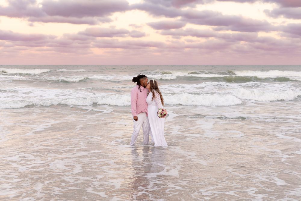 A couple shares an intimate moment while standing in ocean waves at sunset.