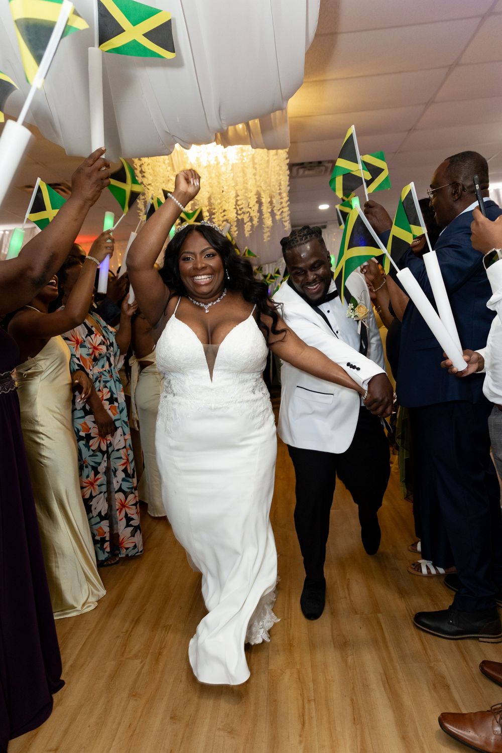 Wedding celebration with guests dancing and waving Jamaican flags on a wooden dance floor.
