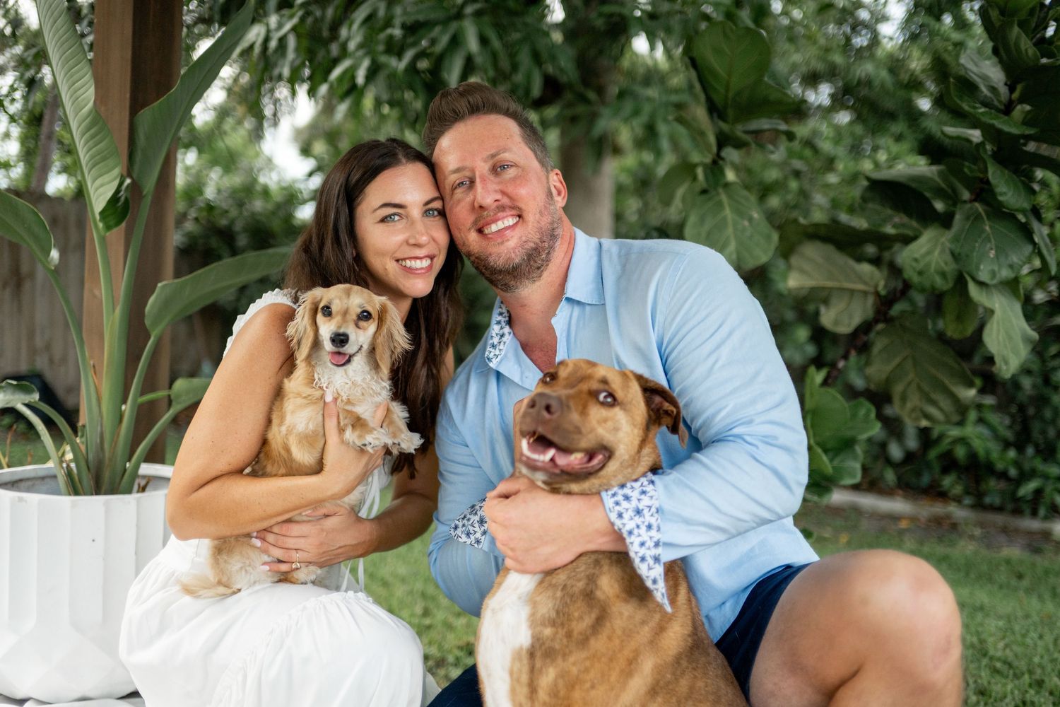 Family portrait in a lush garden setting with their golden retriever dogs.