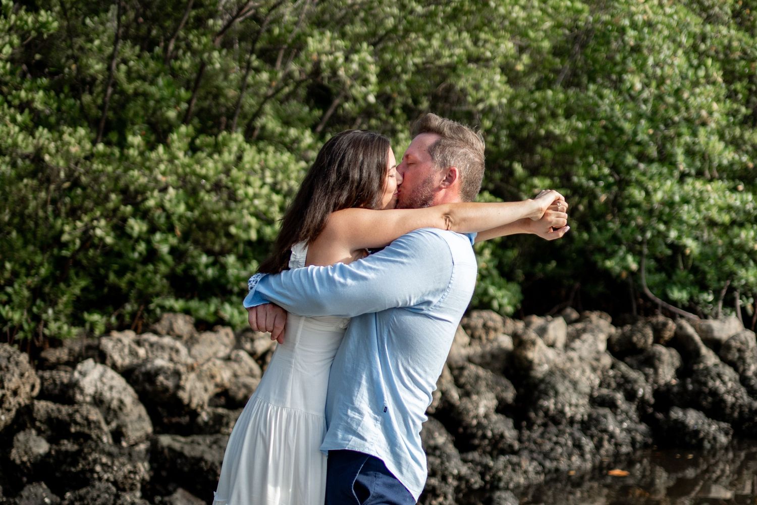 Couple sharing tender moments in a tropical garden setting with natural rock formations.