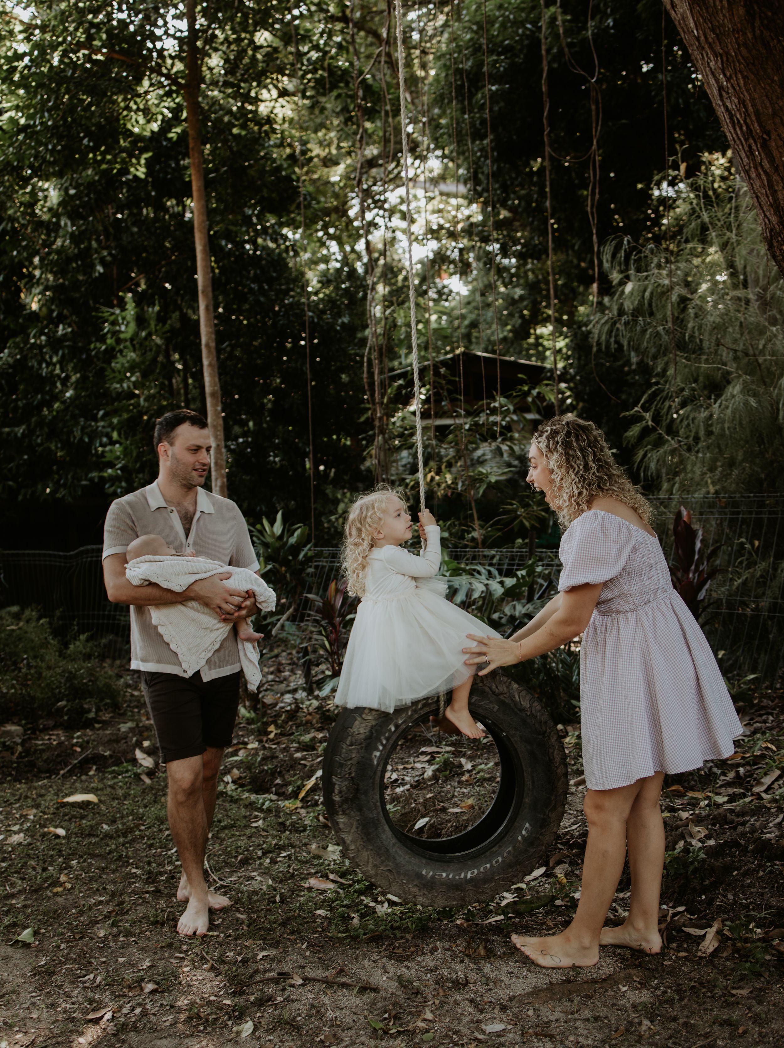 A couple shares playful moments together around a tire swing in a wooded outdoor setting during a photo session.