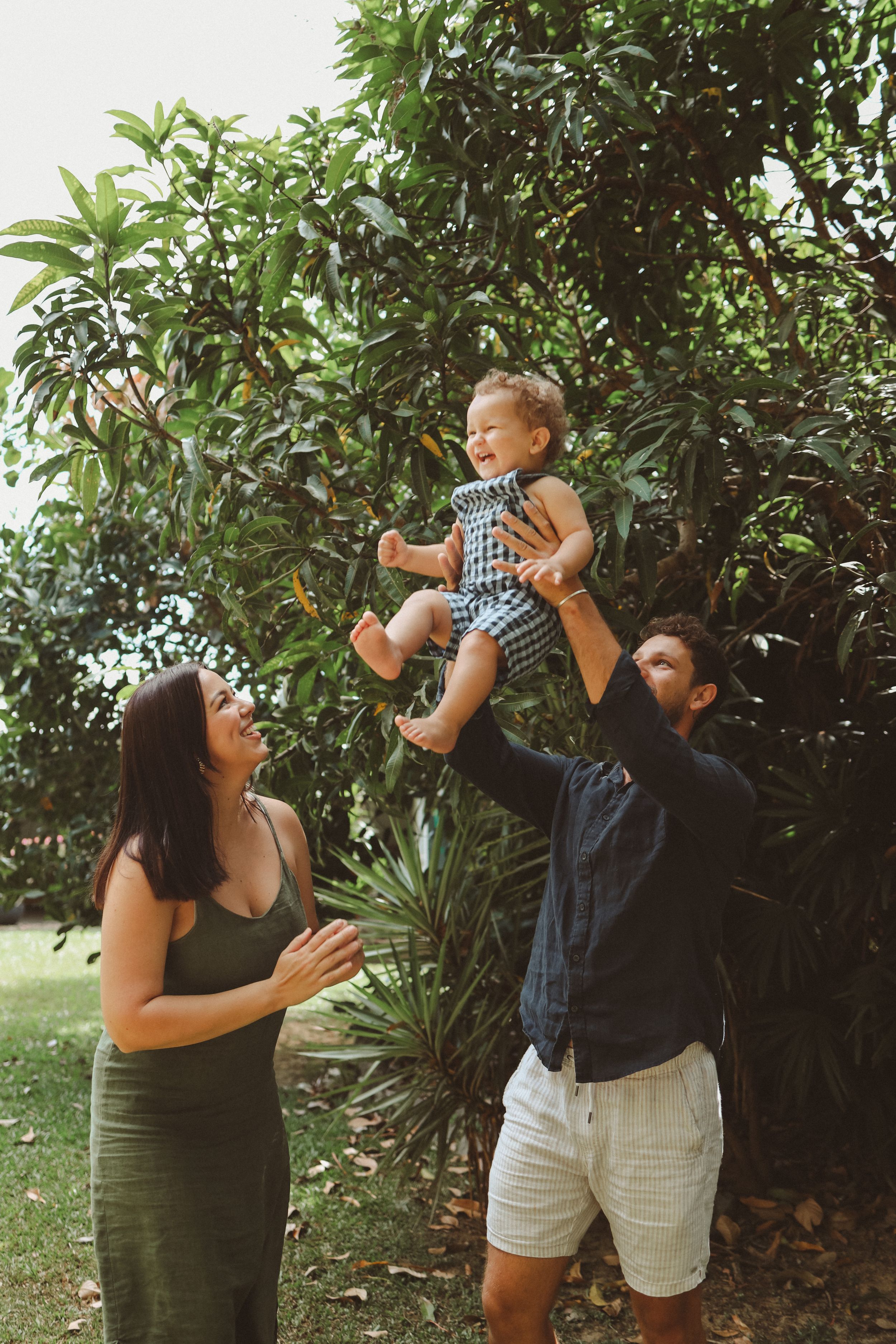 A family enjoying a playful moment together outdoors in a lush garden setting with green foliage in the background.