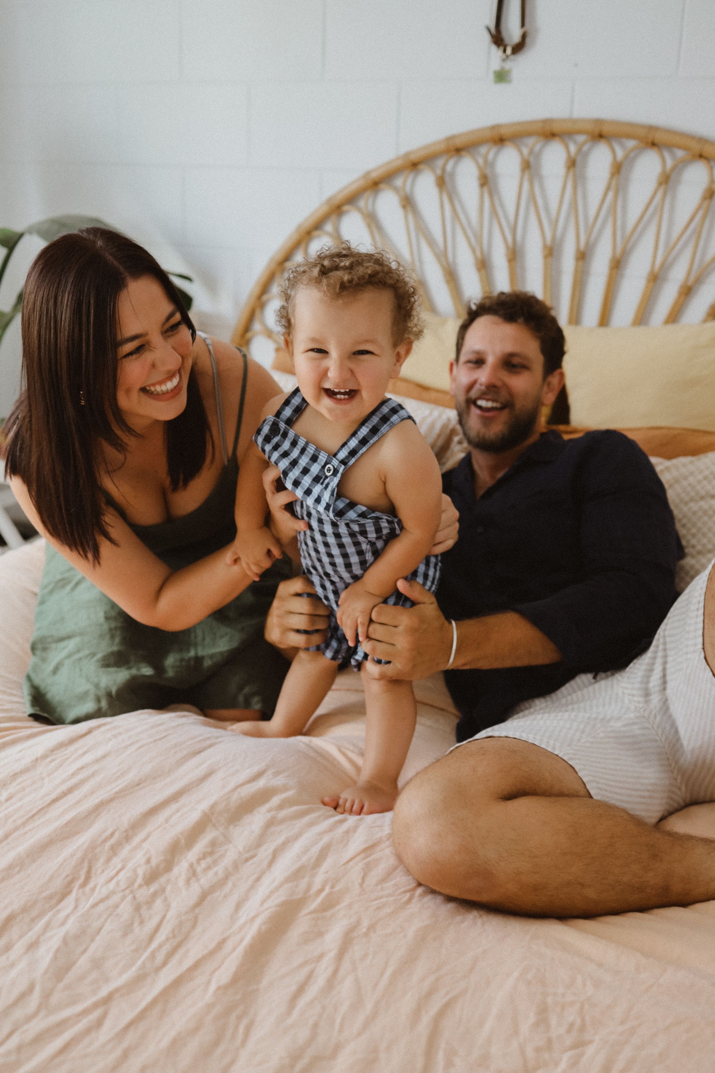 A joyful family moment together on a bed with a rattan headboard, sharing laughter and cuddles.