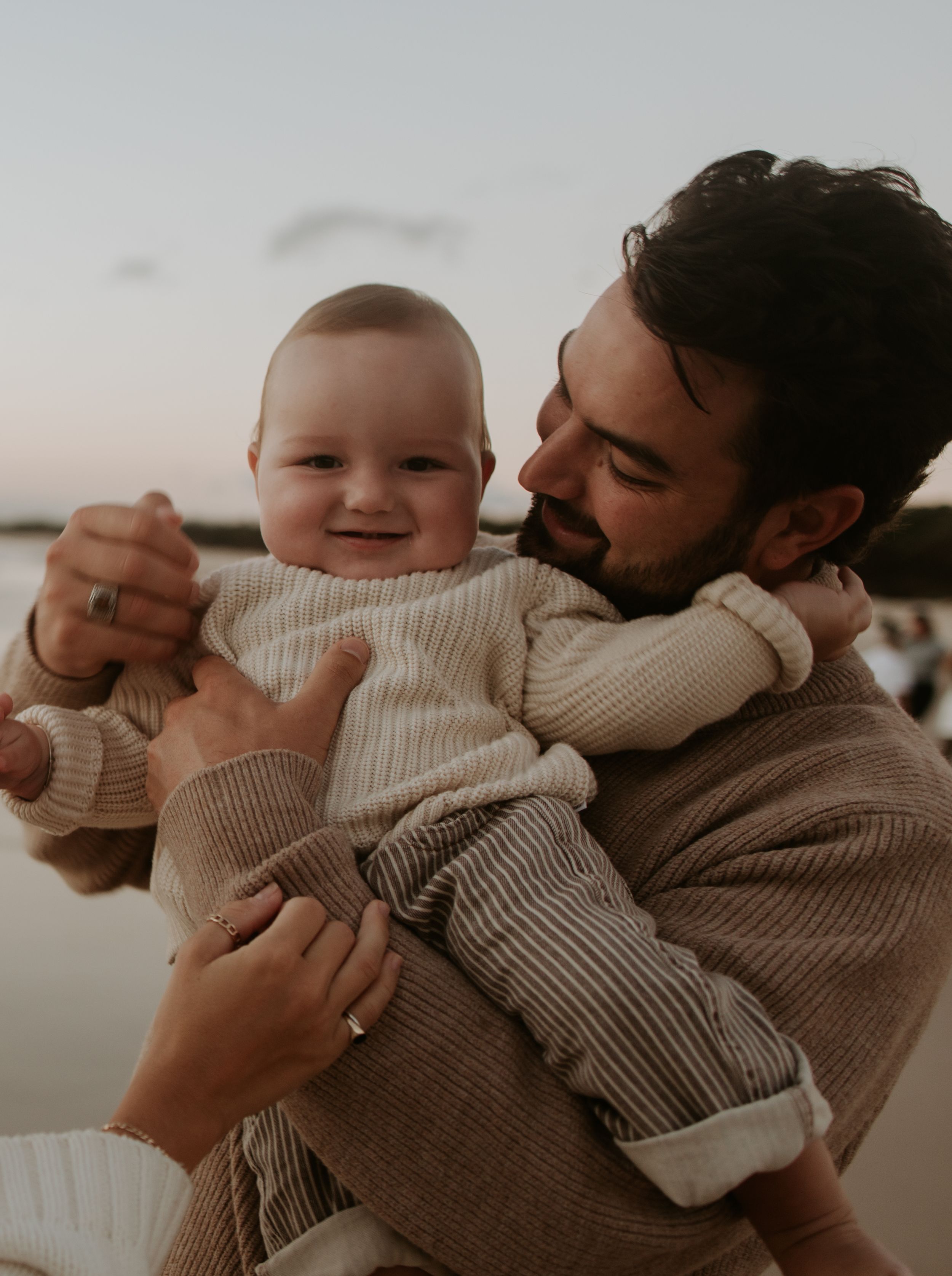 A parent in a beige sweater holds and embraces a baby wearing a cream-colored knit outfit in a tender moment.