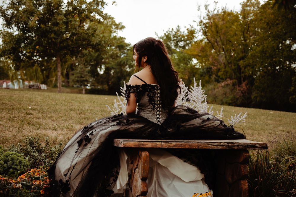 An elegant black and white ballgown photographed on a rustic wooden bench outdoors.