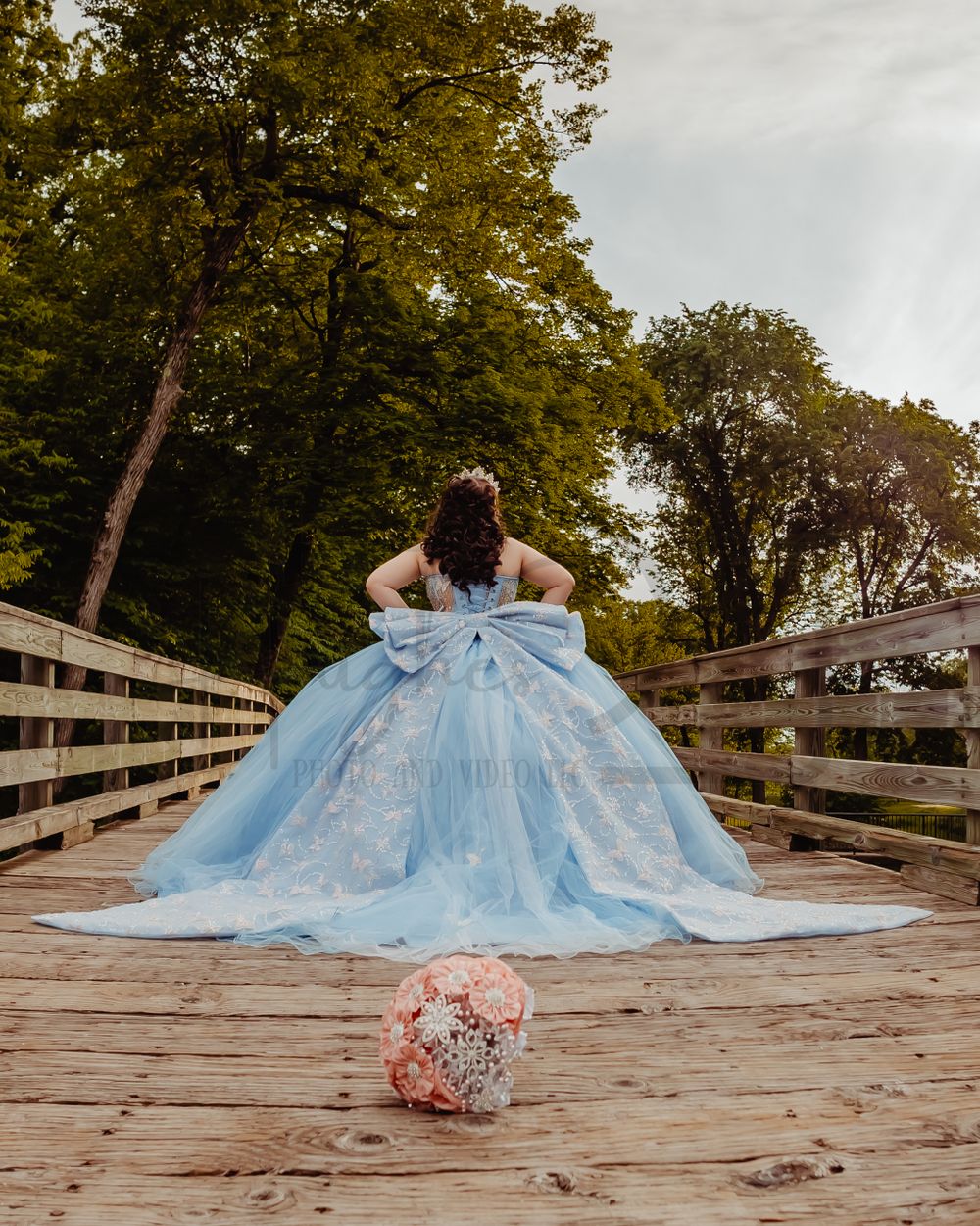A light blue ballgown photographed from behind on a wooden bridge with a pink bouquet on the ground.