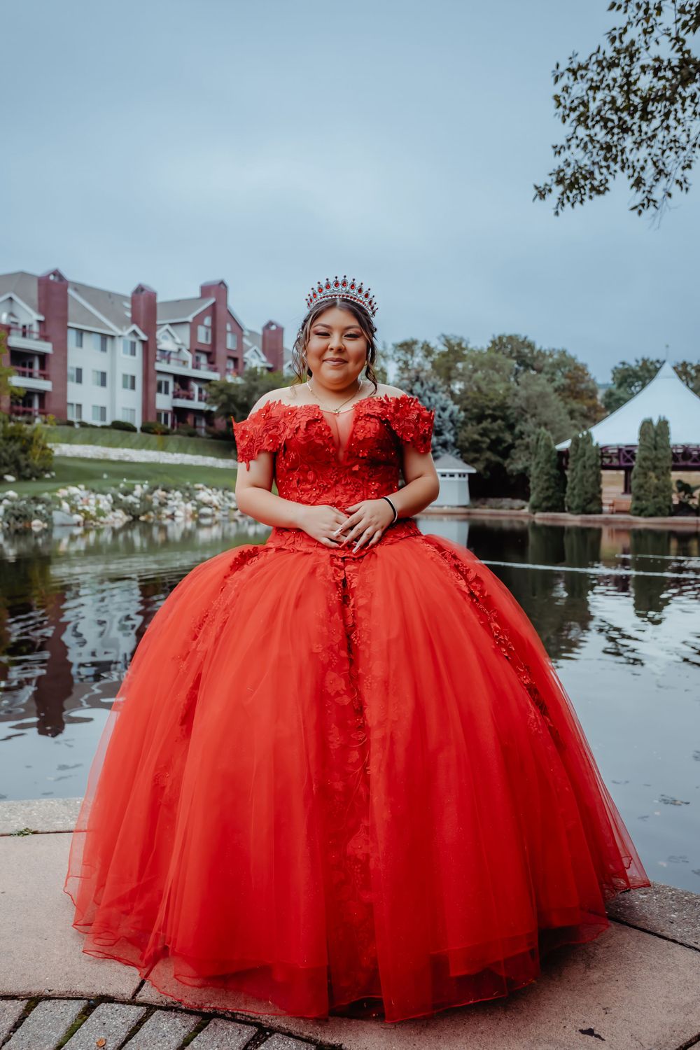 Vibrant red quinceañera dress with floral details photographed by a scenic pond.
