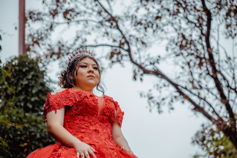 An ornate red quinceañera dress with feather details photographed in an outdoor setting.