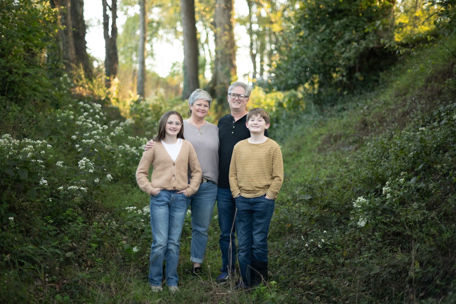 Family portrait of four people standing together on wooded trail during autumn.